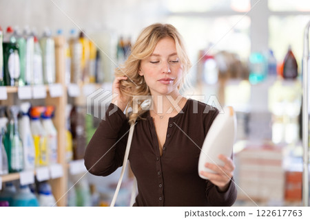 Young woman looking hair care products, standing near shelves in beauty store 122617763
