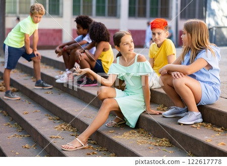 Happy tweenagers friends sitting on steps outdoors and chatting 122617778