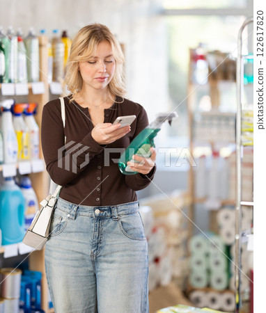 Positive young girl buyer in shop holding and choosing spray, scan QR code 122617820