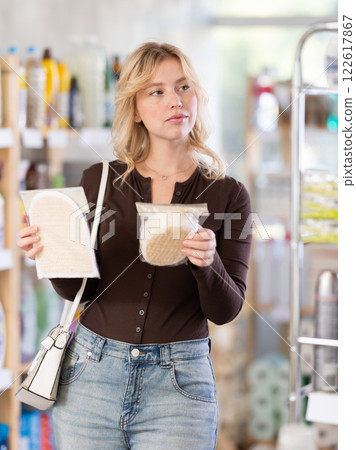 Girl housewife in household store examines goods, chooses washcloth Girl housewife in household store examines goods, chooses washcloth 122617867