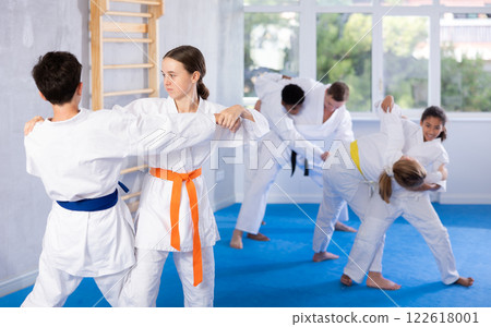 Teen girl honing grappling techniques during kumite with boy at karate training Teen girl honing grappling techniques during kumite with boy at karate training 122618001
