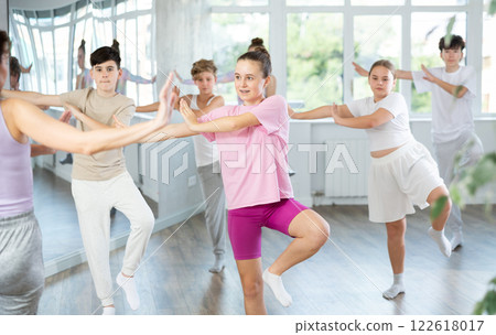 Female girl student repeats movements of unrecognizable teacher during group modern dance class. 122618017
