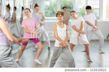 Young girls and boys repeat the movements of dance teacher, training in spacious studio Young girls and boys repeat the movements of dance teacher, training in spacious studio 122618025