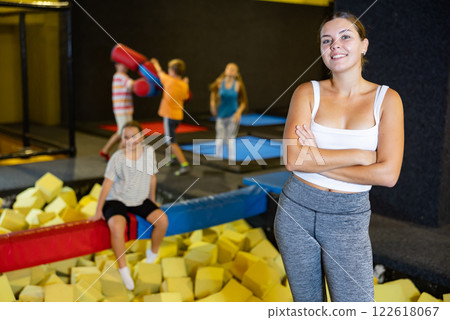 Portrait of happy young European female in white top and gray leggings posing on trampolines foam cube pool in amusement center 122618067