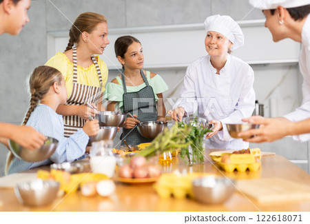 Children are excited to learn how to beat raw eggs with whisk under the guidance of female chef 122618071