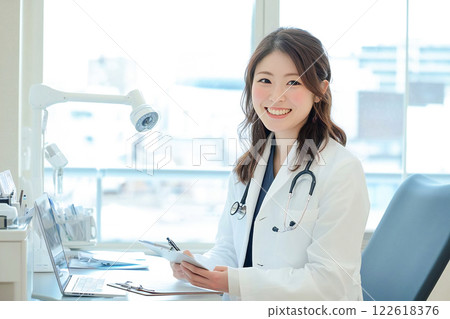 A smiling female doctor checking a patient's chart in the examination room 122618376