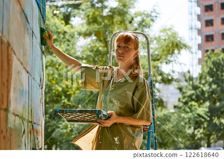 Nice graffiti artist painter with a brush on a stepladder paints a wall Nice graffiti artist painter with a brush on a stepladder paints a wall 122618640