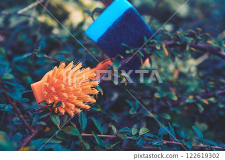 Orange brush,blue sponge for cleaning on green bushes Orange brush,blue sponge for cleaning on green bushes 122619302