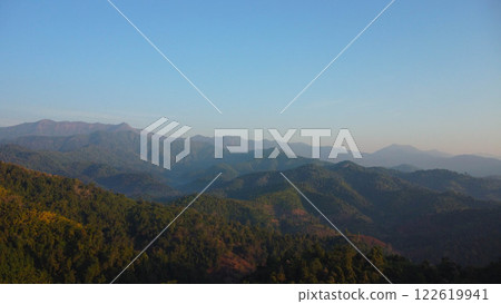 Beautiful sunrise on the mountain with fog in winter. The sun shines down on a serene mountain landscape covered with tropical trees in the early morning. 122619941