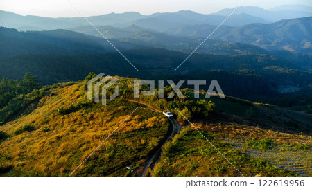 Aerial view of car on rural road driving through tropical forest and mountains in the evening. Aerial view of car on rural road driving through tropical forest and mountains in the evening. 122619956