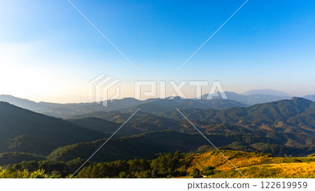 Beautiful sunrise on the mountain with fog in winter. The sun shines down on a serene mountain landscape covered with tropical trees in the early morning. 122619959
