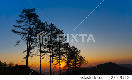 Beautiful sunset in the winter mountains. The setting sun shines down on a serene mountain landscape covered with tropical trees in the evening. 122619960