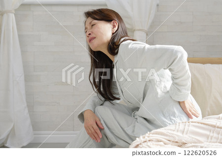Middle-aged woman in pajamas with back pain Middle-aged woman in pajamas with back pain 122620526