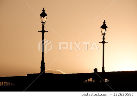 Silhouette of a person crossing a bridge at sunset 122620595