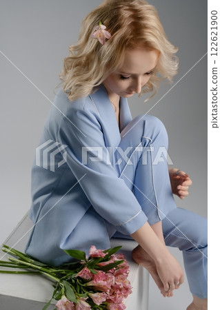 Elegant woman in blue attire sitting with flowers against neutral background Elegant woman in blue attire sitting with flowers against neutral background 122621900