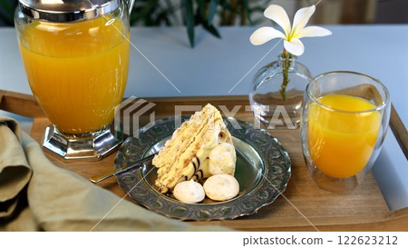 Breakfast setup emphasizes bold contrasts using textured silver plate, golden cake slice, vibrant orange juice in glass, crisp white meringues, presenting geometric minimalist elegance. Breakfast setup emphasizes bold contrasts using textured silver plate, golden cake slice, vibrant orange juice in glass, crisp white meringues, presenting geometric minimalist elegance. 122623212