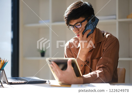 Business professional consulting on phone while using a tablet and reviewing financial documents. 122624978