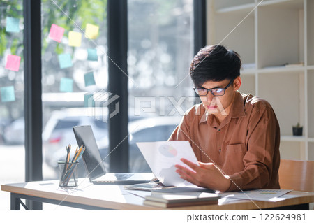 Young businessman analyzing financial data and market trends for investment decisions Young businessman analyzing financial data and market trends for investment decisions 122624981