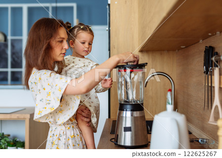 Mother use blender to prepare food with small child in her arms 122625267