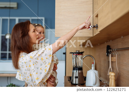 Woman opens kitchen cupboard, takes out food to cook with baby, kitchen furniture Woman opens kitchen cupboard, takes out food to cook with baby, kitchen furniture 122625271