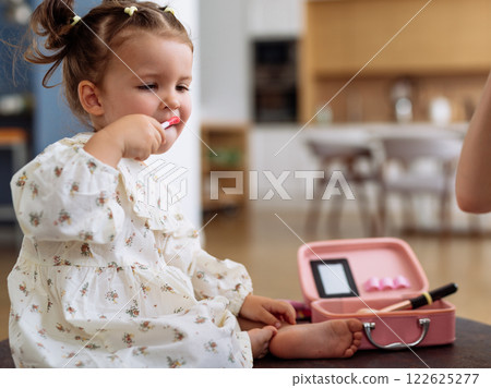 Girl puts on lipstick from a childrens beauty kit 122625277