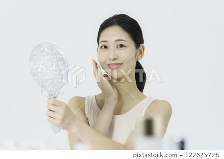 A smiling young woman wearing a tank top on a white background and holding her finger on her cheek Beauty A smiling young woman wearing a tank top on a white background and holding her finger on her cheek Beauty 122625728