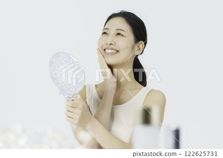 A smiling young woman wearing a tank top on a white background and holding her finger on her cheek Beauty 122625731
