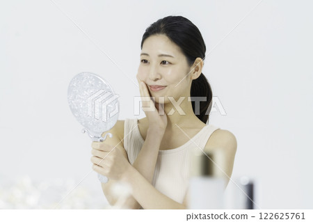 一位身穿背心、面帶微笑的年輕女子，手托著臉頰，看著鏡子裡的美女 122625761