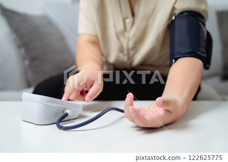 A woman is sitting on a couch with a blood pressure monitor on her arm. She is check blood pressure A woman is sitting on a couch with a blood pressure monitor on her arm. She is check blood pressure 122625775