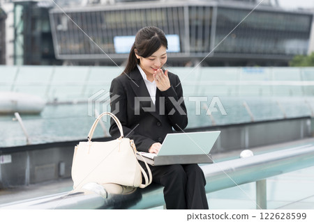 A smiling businesswoman looking at a laptop outdoors at the Water Spaceship, OASIS21, Sakae, Nagoya 122628599