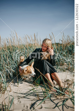 A woman enjoys a sunny day at the beach while hugging her corgi in the tall grass A woman enjoys a sunny day at the beach while hugging her corgi in the tall grass 122630322