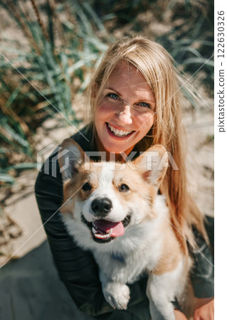 Happy Woman Holding a Smiling Corgi on a Sunny Day 122630326