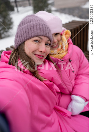 Mother and Her Adorable Daughter Joyfully take selfie in Winter Wonderland While Wearing Bright Pink Coats 122630385