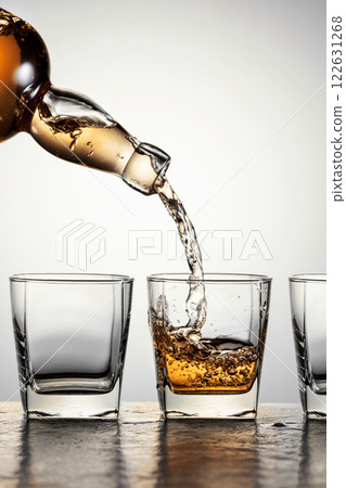 Whiskey is poured from a bottle into a glasses. 122631268