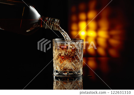 Pouring whiskey from a bottle into a glass with ice. Pouring whiskey from a bottle into a glass with ice. 122631310