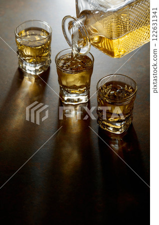 Whiskey poured from a decanter into a small glasses. 122631341