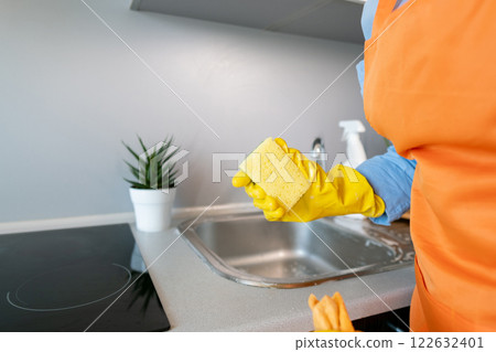 A woman holds a cleaning sponge; a clean sink prevents dirt and bacteria buildup, supporting overall hygiene and health at home. A woman holds a cleaning sponge; a clean sink prevents dirt and bacteria buildup, supporting overall hygiene and health at home. 122632401