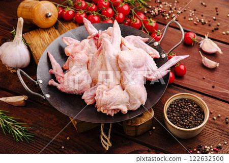 Fresh chicken wings surrounded by herbs and vegetables on a rustic wooden table in a kitchen setting 122632500