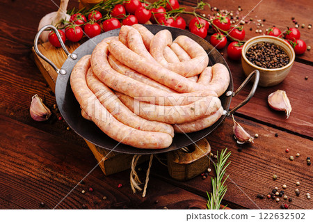 Freshly made sausages on a rustic wooden table with tomatoes and spices nearby Freshly made sausages on a rustic wooden table with tomatoes and spices nearby 122632502