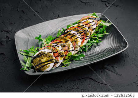 Freshly prepared salad with pesto, grilled vegetables, and arugula served on a sleek black plate Freshly prepared salad with pesto, grilled vegetables, and arugula served on a sleek black plate 122632563