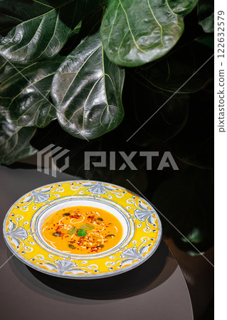 Spicy soup served in vibrant yellow dish surrounded by lush greenery in a cozy setting 122632579