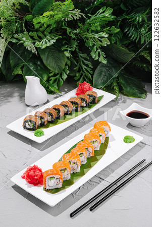 Fresh sushi rolls arranged on elegant plates with garnishes in a tranquil setting surrounded by greenery 122632582