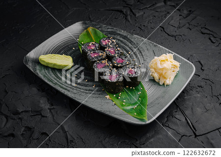 Fresh sushi rolls served on a stylish black plate with garnishes in a modern dining setting Fresh sushi rolls served on a stylish black plate with garnishes in a modern dining setting 122632672
