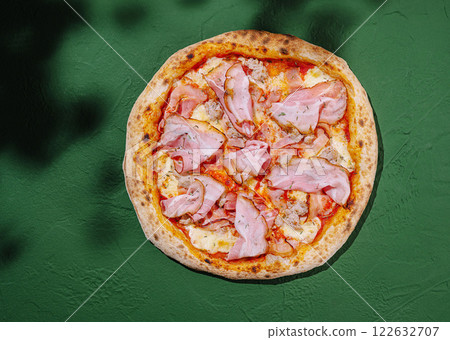 Delicious ham pizza on a vibrant green surface showcasing a classic Italian dish ideal for any meal 122632707