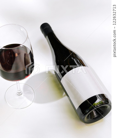 Dark red wine in glass next to an elegantly presented bottle on a neutral background Dark red wine in glass next to an elegantly presented bottle on a neutral background 122632713