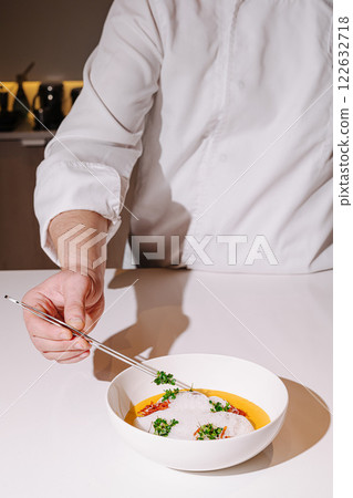 Culinary artist plating a gourmet dish with precision in a modern kitchen at twilight 122632718