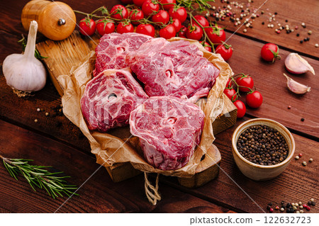 Fresh cuts of meat arranged on a wooden board with herbs, spices, and cherry tomatoes ready for cooking 122632723