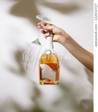 Hand holding a bottle of rose wine and an empty glass with a floral label in soft lighting 122632727