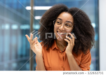 Smiling woman having phone conversation in modern office. Wearing glasses and orange shirt, appears happy, engaged, showcasing concept of communication, connection, technology, and business setting. Smiling woman having phone conversation in modern office. Wearing glasses and orange shirt, appears happy, engaged, showcasing concept of communication, connection, technology, and business setting. 122632731