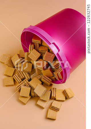Waffle biscuit pieces spilled from a pink container on a peach-colored surface Waffle biscuit pieces spilled from a pink container on a peach-colored surface 122632745